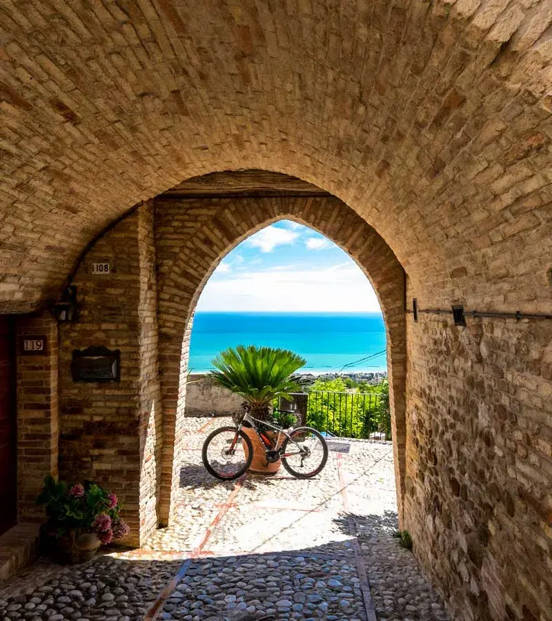 Una bicicletta sotto un arco in mattoni che si apre sul mare