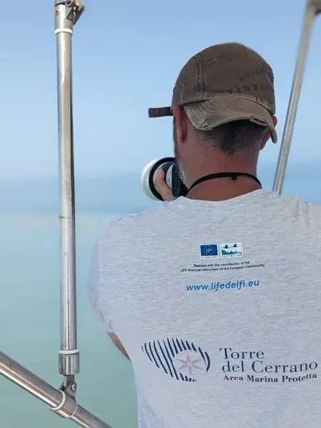 Un fotografo di spalle sulla barca, con la maglietta dell’Area Marina Protetta Torre del Cerrano