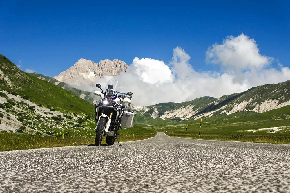 Una moto ferma su una strada di montagna, tra prati e cime rocciose